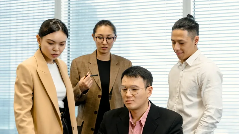 Four colleagues in an office reviewing a laptop together during a Magento to WooCommerce migration assessment